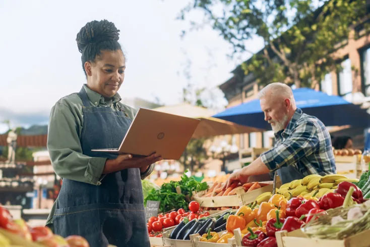 A farmer’s market setting where a woman is using her laptop.